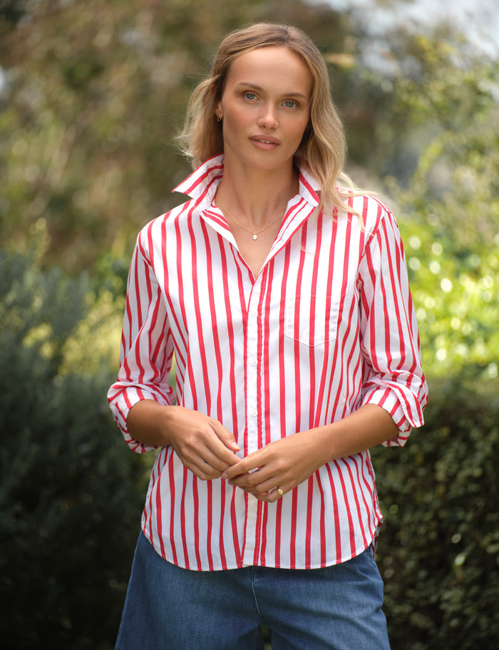 Woman wearing a red and white striped shirt outdoors with greenery in the background