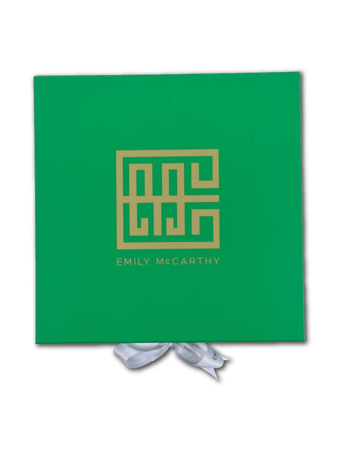 The Emily McCarthy Gift Box is green with a gold geometric logo and EMILY McCARTHY in gold. A partially visible white ribbon adds a luxe touch at the bottom.