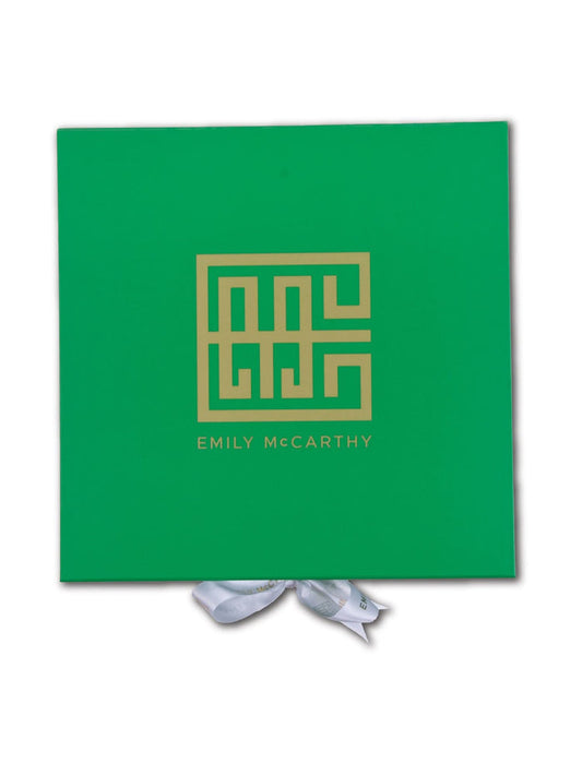 The Emily McCarthy Gift Box is green with a gold geometric logo and EMILY McCARTHY in gold. A partially visible white ribbon adds a luxe touch at the bottom.