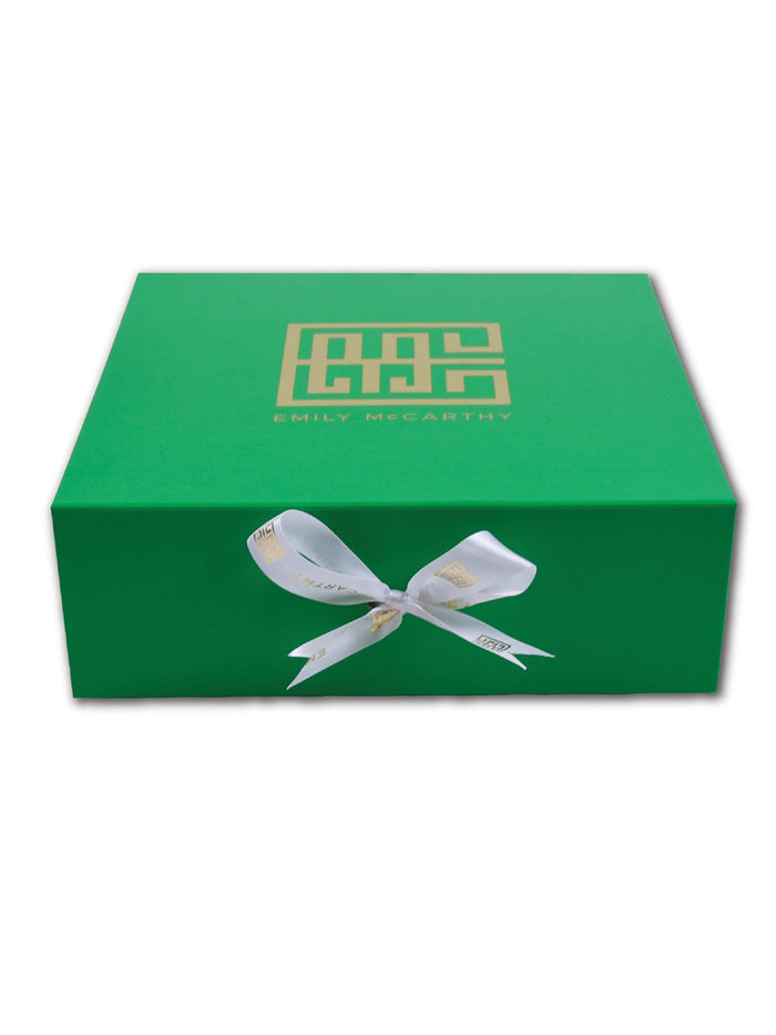 The Emily McCarthy Gift Box is a rectangular green box with a gold geometric logo and Emily McCarthy on the lid, tied with a white ribbon, presented against a crisp white background.