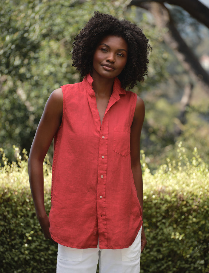 Woman wearing a red sleeveless shirt standing outdoors with greenery in the background