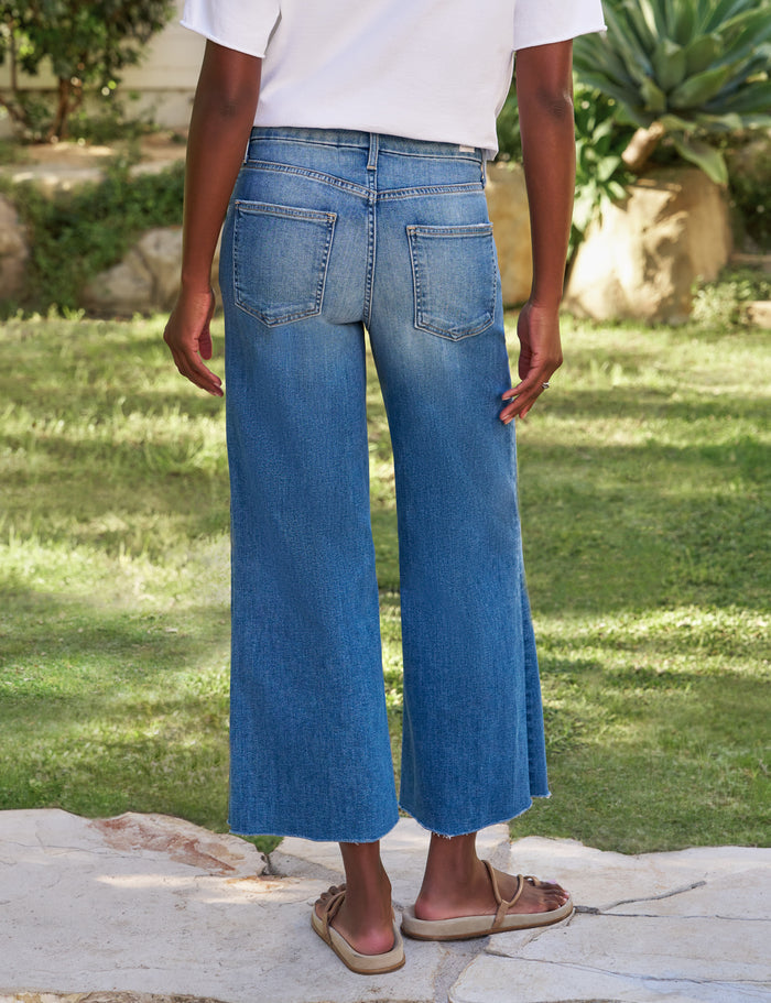 Person wearing blue jeans standing on a stone path with grass and plants in the background