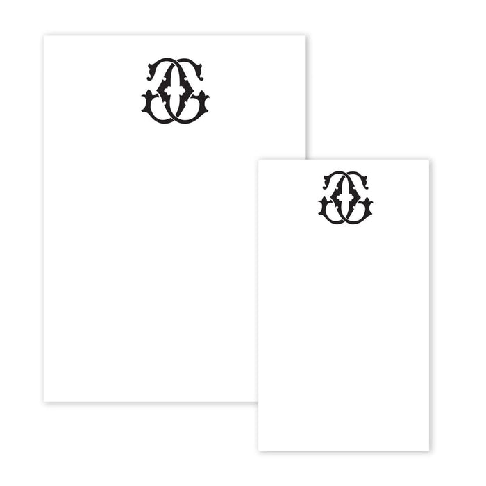 The Gift Bar Notepad Set includes two white notepads of different sizes, each adorned with a symmetrical decorative black emblem at the top center, resembling a stylized letter A. The pages are otherwise blank.