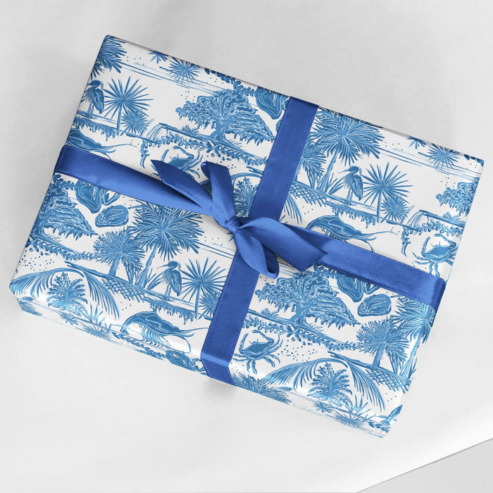 The product, Gift Wrap - Low Country, features a tropical jungle design in blue and white with trees and animals. It is adorned with a blue ribbon tied into a bow and is set against a white surface.