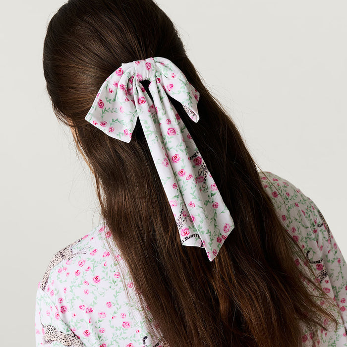 Person with long hair wearing a floral ribbon in a ponytail against a plain background
