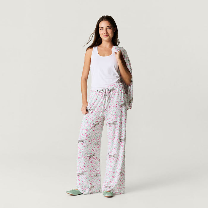 Woman wearing a white tank top and floral pants on a plain background
