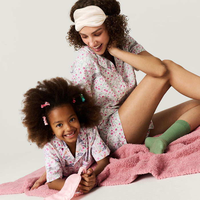 Woman and child in matching pajamas sitting on a pink blanket.