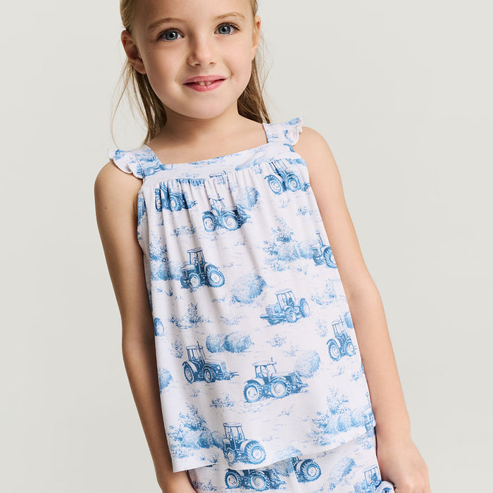 Young girl wearing a sleeveless top with blue tractor pattern on a plain background