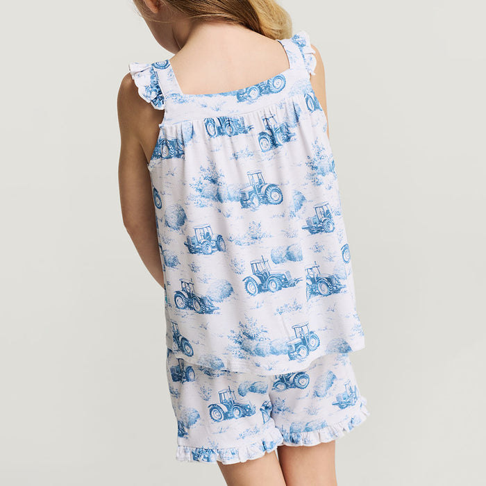 Child wearing a white dress with blue tractor pattern on a plain background