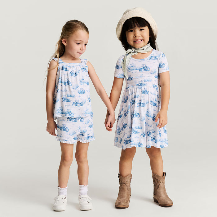 Two children wearing matching blue and white floral dresses on a plain background