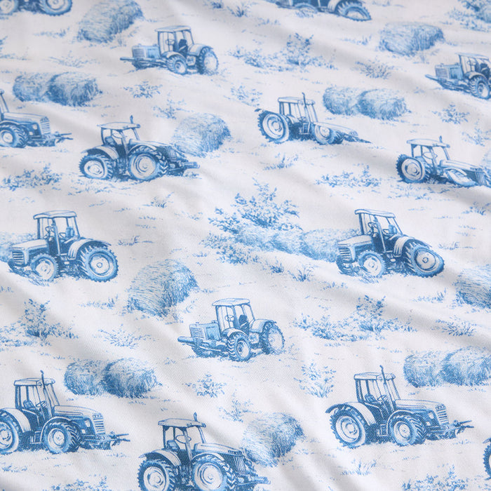 Pattern of blue tractors and hay bales on a white fabric background