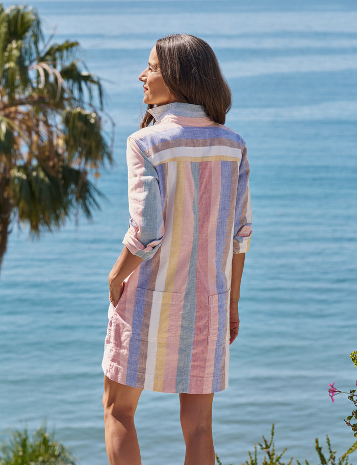 Woman wearing a colorful striped dress standing by a body of water with palm trees.