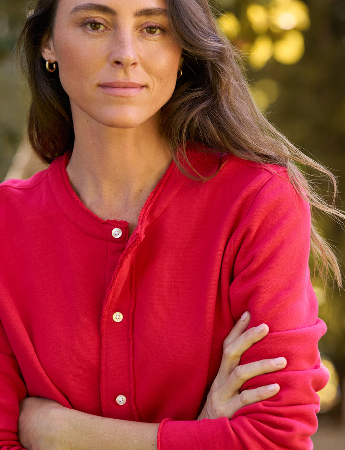 A woman wearing a bright red long-sleeve button-front top, photographed outdoors with a softly blurred natural background.