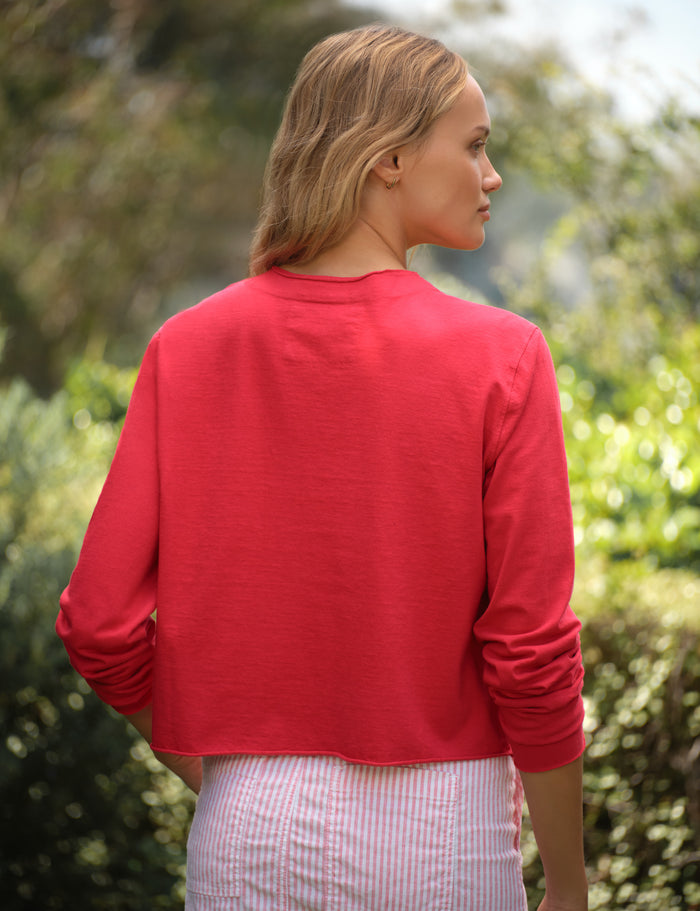 Woman wearing a red cardigan and striped skirt standing outdoors with greenery in the background