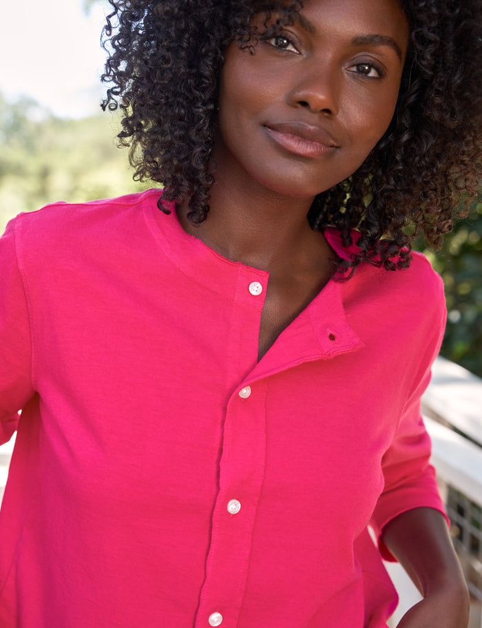 Woman wearing a bright pink shirt with a blurred outdoor background