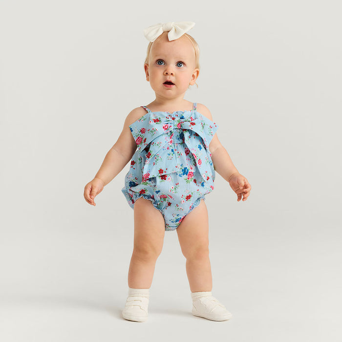 Baby wearing a floral romper with a bow on a light gray background