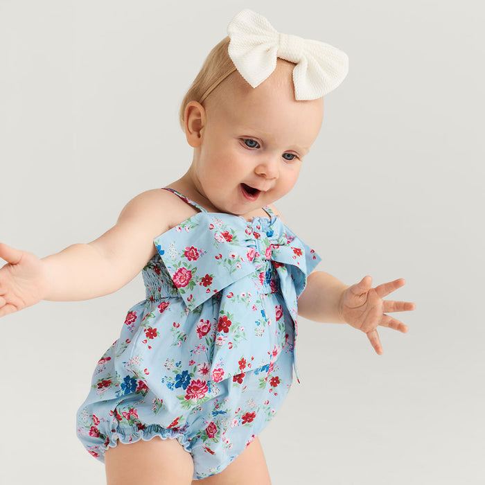 Baby wearing a floral romper with a large bow on a plain background