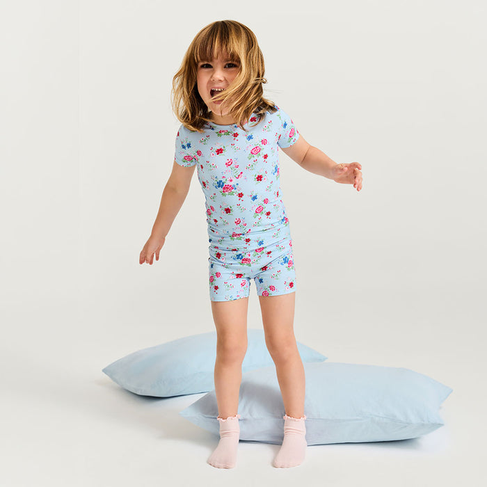Child wearing a floral pajama set on light blue pillows against a white background