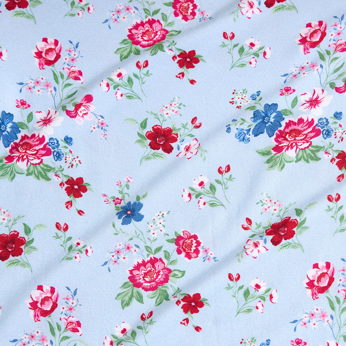 Floral fabric pattern with red, pink, and blue flowers on a light blue background