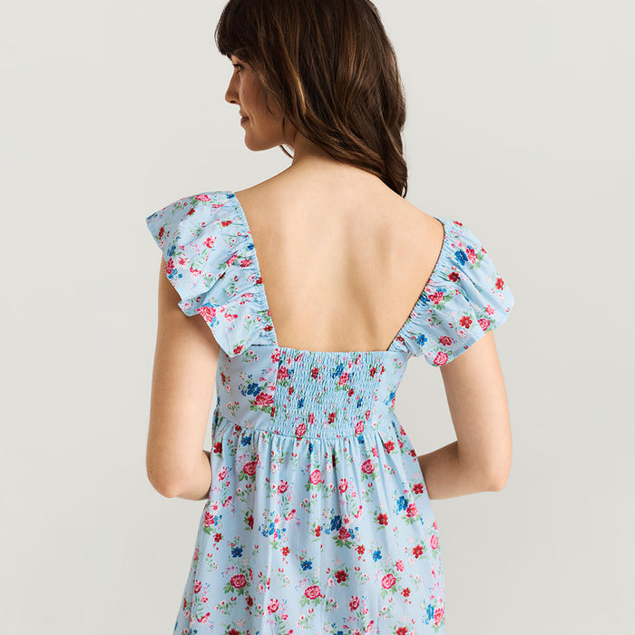 Woman wearing a light blue floral dress with ruffled sleeves on a plain background