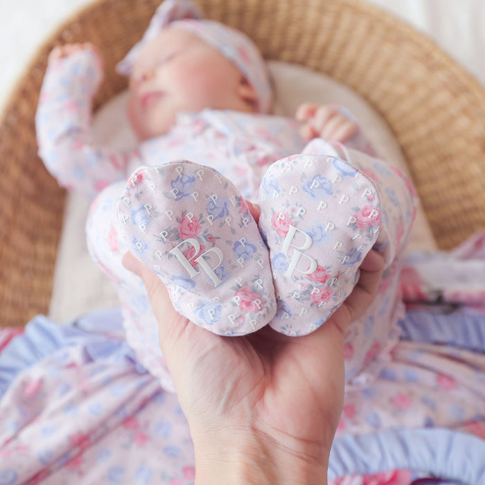 Baby's feet with 'PP' initials held by a hand, wearing a patterned outfit.