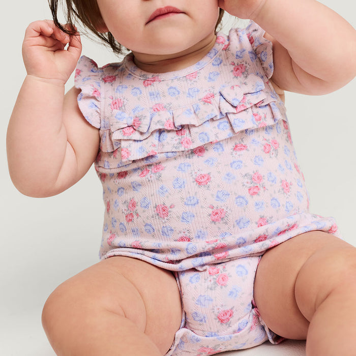 Baby wearing a floral bubble romper on a plain background