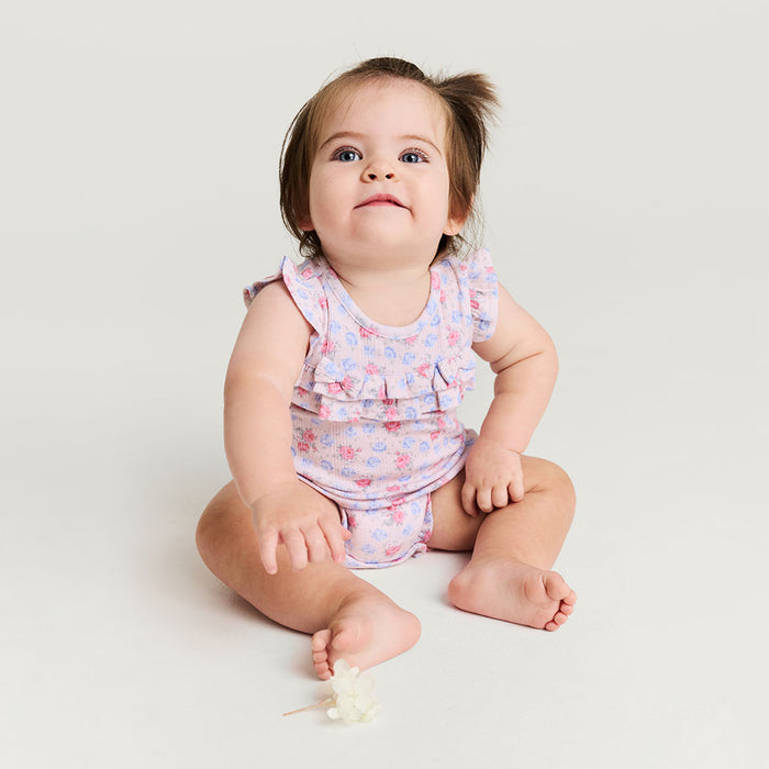 Baby sitting on a white surface wearing a floral romper.