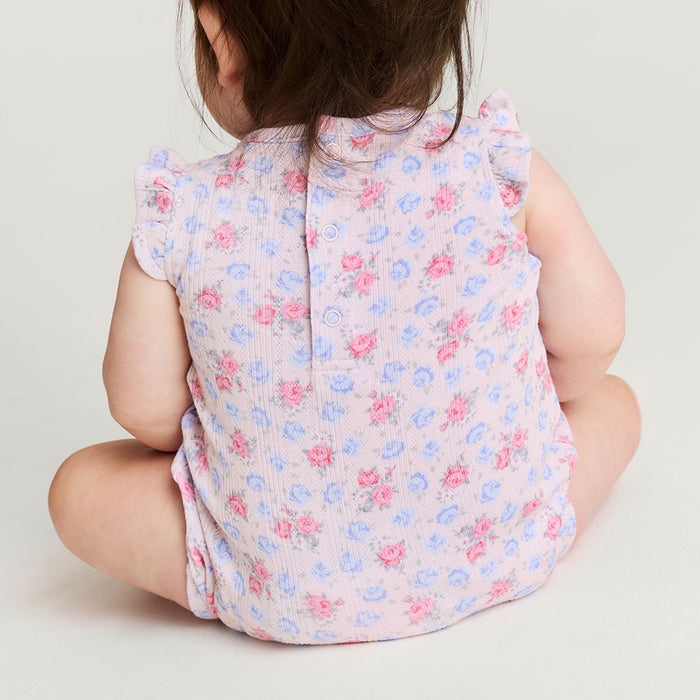 Child wearing a floral romper sitting on a white background