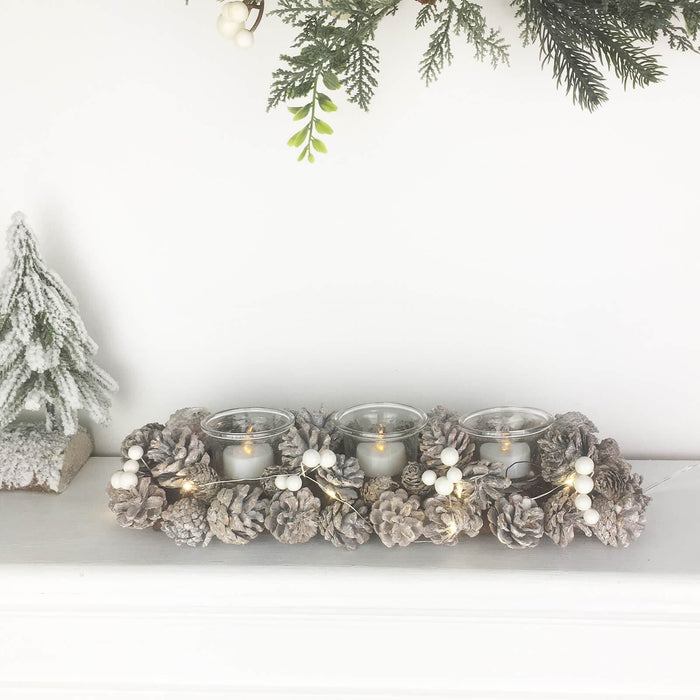 Decorative candle holder with pinecones and candles on a white surface with Christmas decorations.