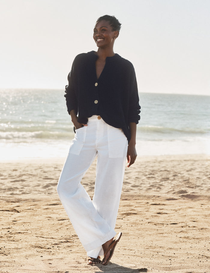 Woman standing on a beach wearing a navy cardigan and white pants.