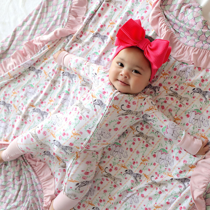 Baby in a patterned outfit with a large pink bow on a matching blanket