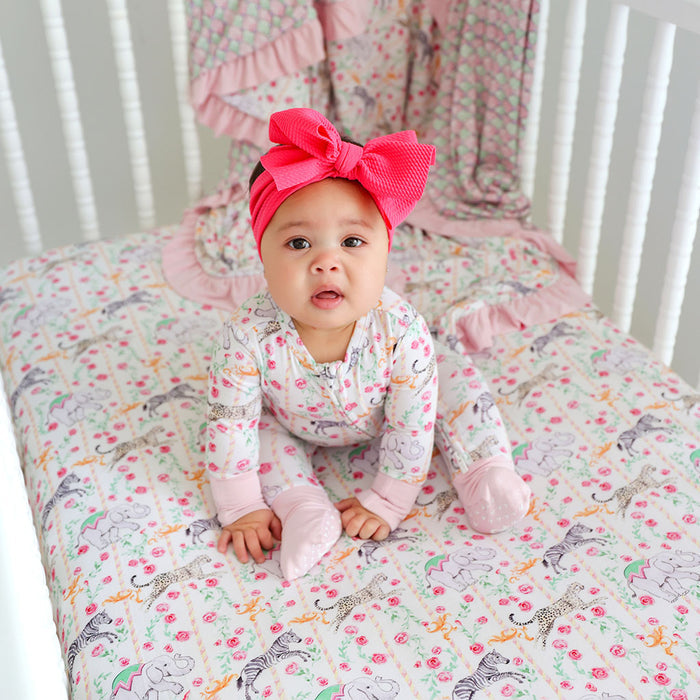 Baby in a crib with a colorful sheet and pink headband