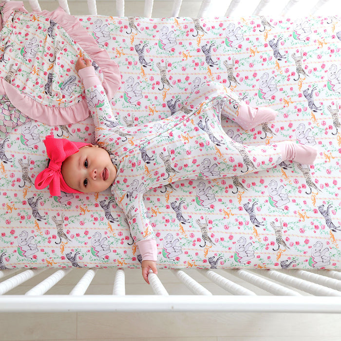 Baby lying on a crib with a colorful patterned sheet and pink headband.