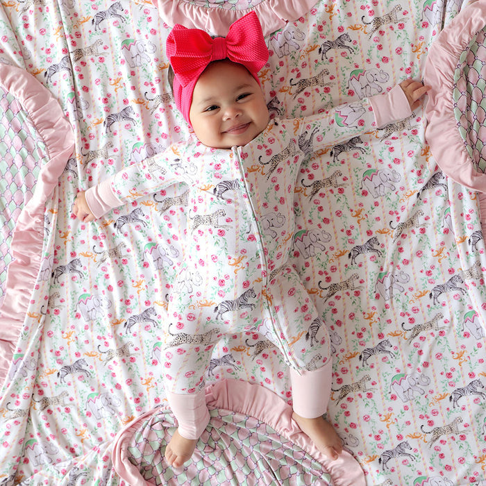 Baby in a patterned one piece with a large red bow on a matching crib sheet.