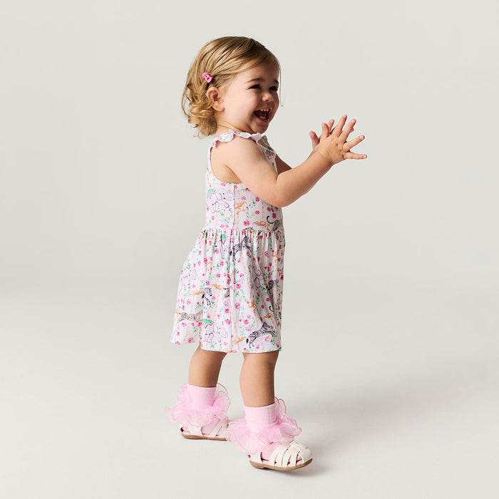 Child wearing a floral dress and pink sandals on a plain background