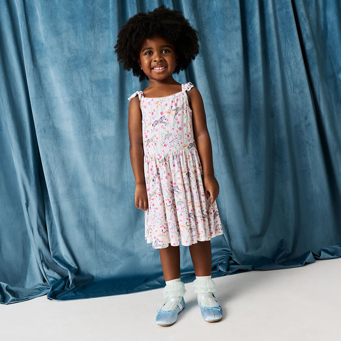Child wearing a white dress with flowers and animal print against a blue velvet curtain