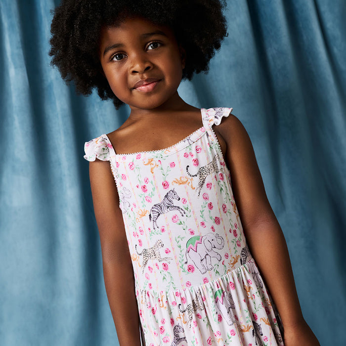 Young girl wearing a floral dress with animal prints against a blue curtain background