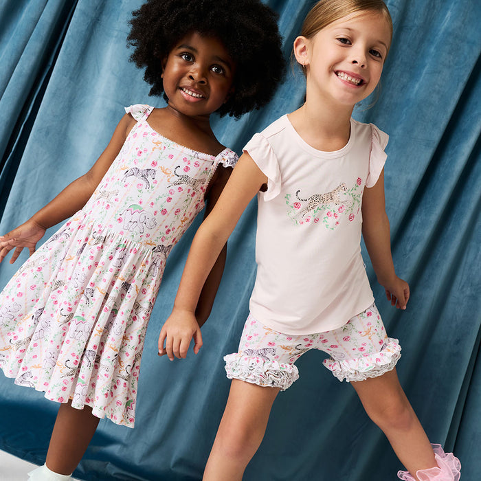 Two young girls wearing matching outfits with floral patterns against a blue curtain background.
