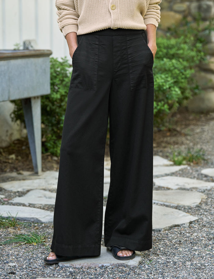 Person wearing black wide-leg pants and a beige cardigan standing outdoors.