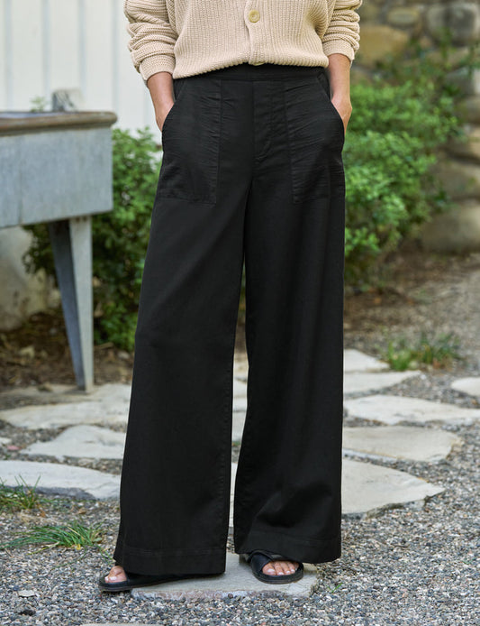 Person wearing black wide-leg pants and a beige cardigan standing outdoors.
