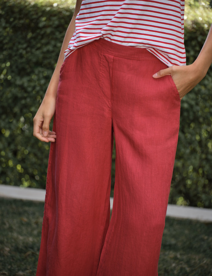 Person wearing red pants and a striped shirt against a green hedge background