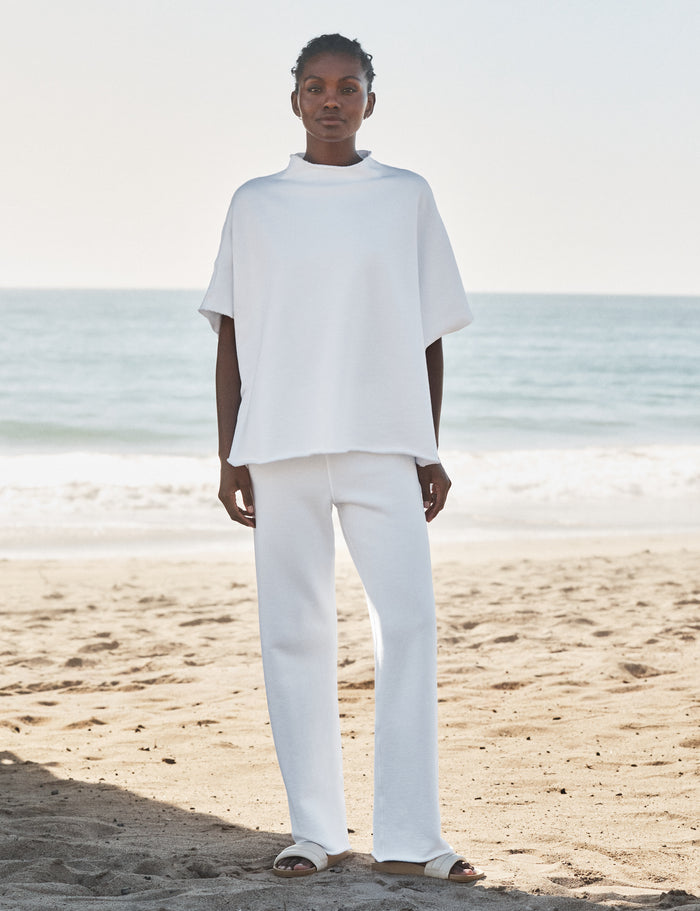 Person wearing a white outfit standing on a beach with ocean in the background