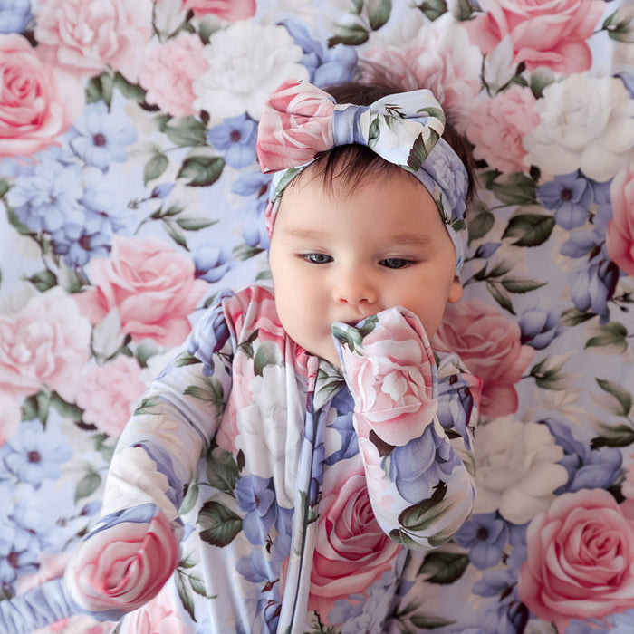 Baby wrapped in a floral blanket with a matching headband on a floral background