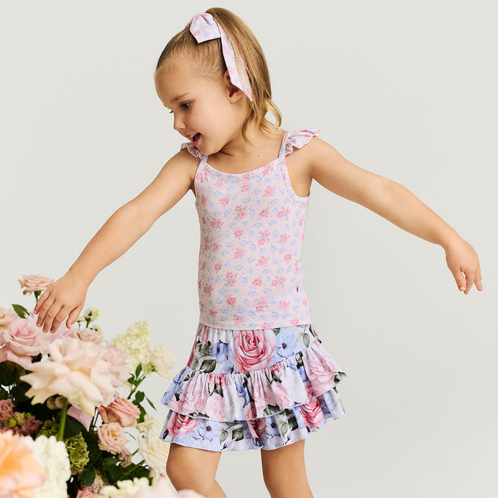 Young girl in a floral skirt standing next to flowers on a light background