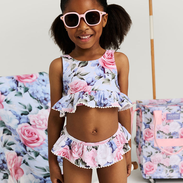 Young girl wearing a floral two-piece outfit with sunglasses, standing in front of floral-patterned Hulken bag.