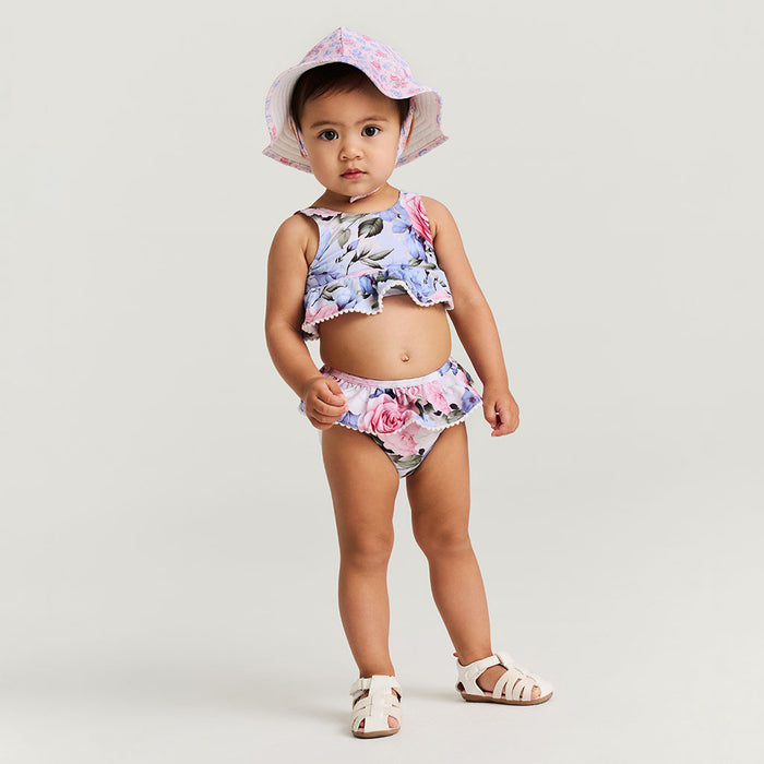 Child wearing a floral two piece swimsuit and hat on a plain background