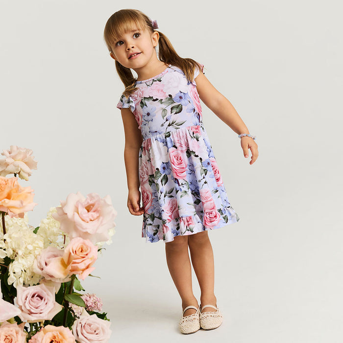 Young girl in a floral dress standing next to flowers on a white background