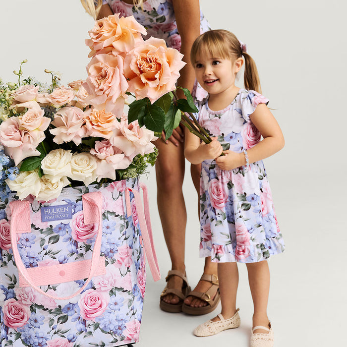 Woman and young girl in floral outfits holding flowers next to a floral bag.