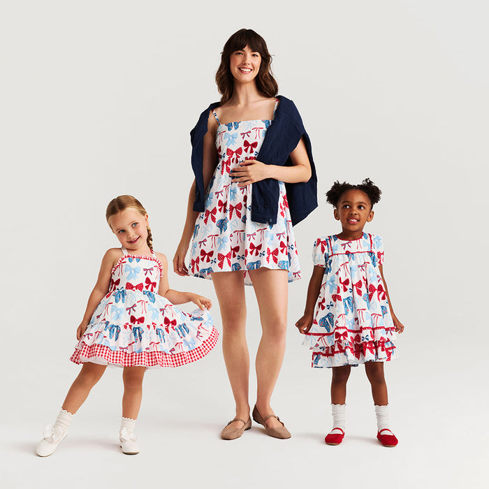 Woman and two children wearing matching dresses with a pattern of blue and red bows on a white background.