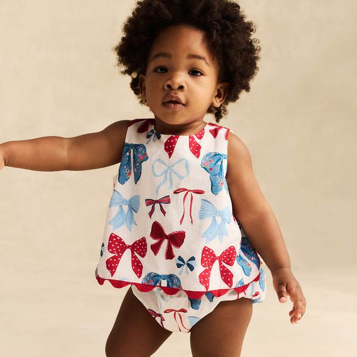 Child wearing a sleeveless top with bow pattern on a beige background